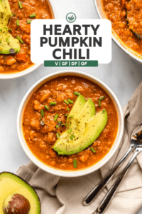 two bowls of pumpkin chili topped with avocado and chives next to pot of chili