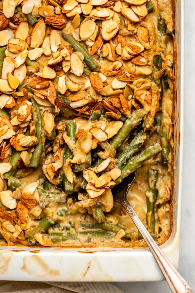 baked green bean casserole with serving spoon scooping a serving out of white casserole dish