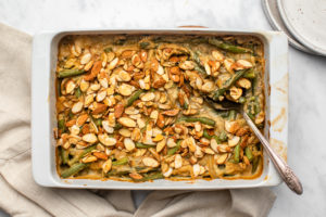 green bean casserole in white casserole dish with silver serving spoon