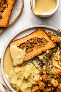 photo of slice of holiday roast on plate with mashed potatoes, gravy, green bean casserole, and stuffing