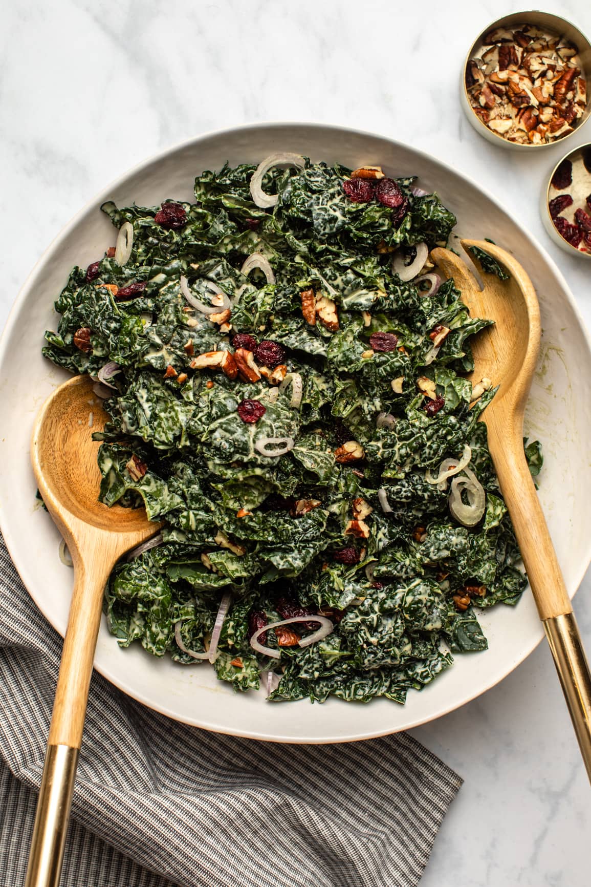 massaged kale cranberry salad in large white bowl with wooden serving spoons