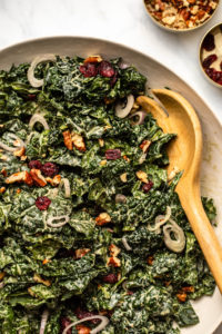 kale & cranberry salad in large white serving bowl with wooden spoon
