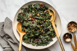kale & cranberry salad tossed in tahini cider dressing in large white bowl topped with pecans and shallot