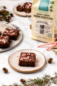 candy cane brownies on white serving plate surrounded by fresh garland and bag of brown rice flour