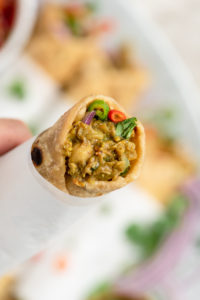 hand holding chana kathi roll wrapped in parchment paper with focus on chickpea curry filling