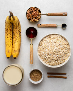 ingredients for banana bread baked oatmeal in measuring cups on white background