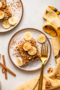 slice of baked banana bread oatmeal on small white plate topped with sliced banana and cinnamon