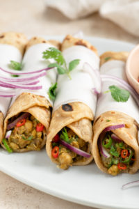 chana kathi rolls wrapped in parchment paper on plate topped with red onion and cilantro