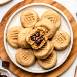 stack of peanut butter cookies stuffed with chocolate on white plate next to glass of non-dairy milk