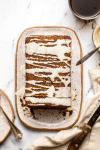 gingerbread loaf drizzled in icing sugar on white serving tray next to bowl of icing sugar