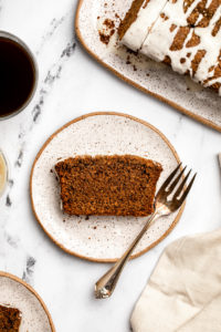 slice of gingerbread loaf on small white plate next to cup of coffee and rest of gingerbread loaf on white serving tray