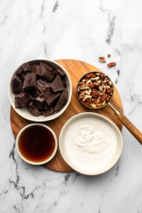 white bowls of coconut cream, chocolate, maple syrup, and pecans on wood cutting board