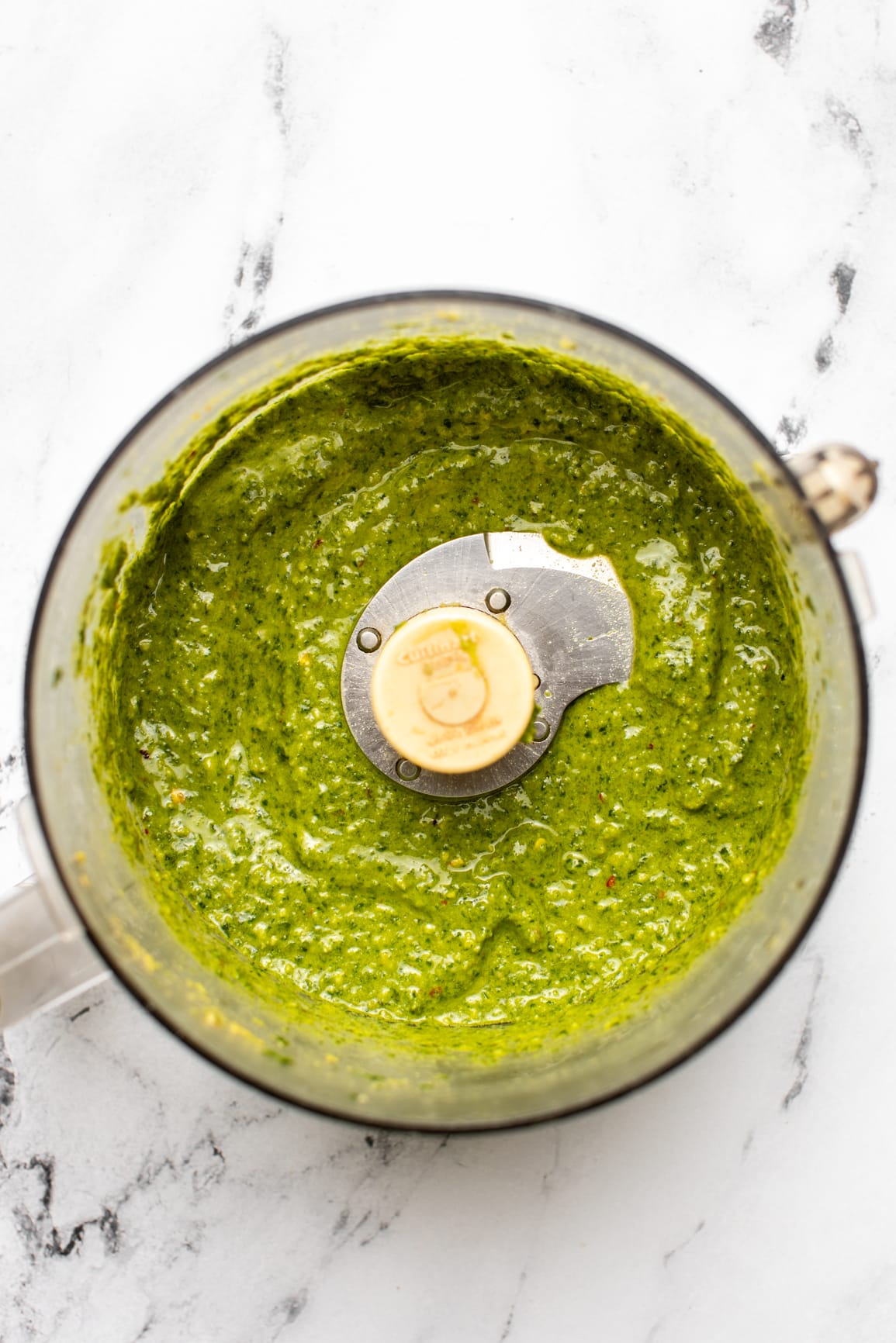 blended pesto in food processor container on marble countertop