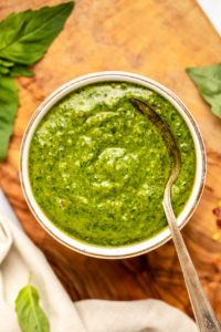 close up photo of white bowl of pesto on cutting board with spoon in bowl