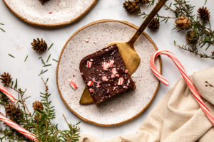 two candy cane brownies on small white plates on marble countertop with holiday decorations