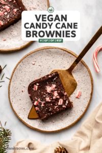 two candy cane brownies on small white plates on marble countertop with holiday decorations