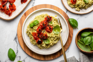 plate of pesto risotto topped with tomatoes on wood cutting board on marble countertop