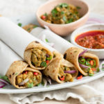 chana kathi rolls wrapped in parchment paper on white serving plate next to tomato and mint chutney