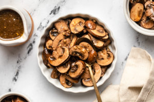 balsamic marinated mushrooms in white bowl on marble background