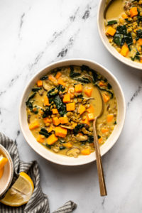 bowl of coconut curry lentil soup with gold spoon on marble background