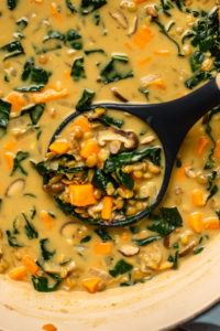 close up photo of soup ladle scooping out some coconut curry lentil soup with sweet potato, shiitake mushrooms, and kale