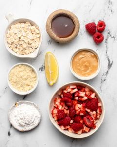 ingredients for two person berry crumbles arranged in small white ramekins on marble background