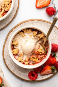 vegan berry crumble topped with scoop of melting vanilla ice cream with gold spoon in bowl