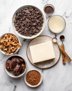 small bowls of chocolate chips, walnuts, dates, cacao powder, tofu, milk, coffee, vanilla, and salt on marble background
