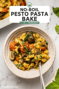 no boil pesto pasta bake with mushrooms and tomatoes served in a white speckled bowl topped with fresh basil on marble background