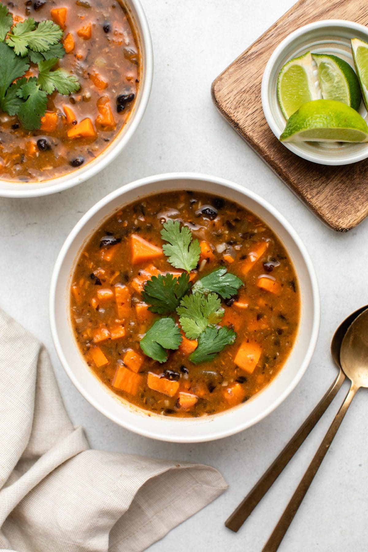 two bowls of black bean sweet potato soup topped with cilantro with lime wedges on the side 
