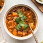 bowl of chipotle black bean sweet potato soup topped with cilantro with lime wedges on the side