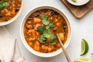 bowl of chipotle black bean sweet potato soup topped with cilantro with lime wedges on the side