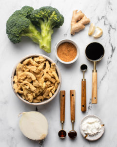 soy curls, broccoli, and half an onion arranged with sauce ingredients on marble countertop