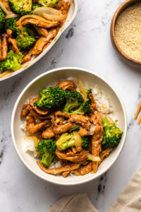 vegan beef and broccoli over white rice in white bowl on marble countertop
