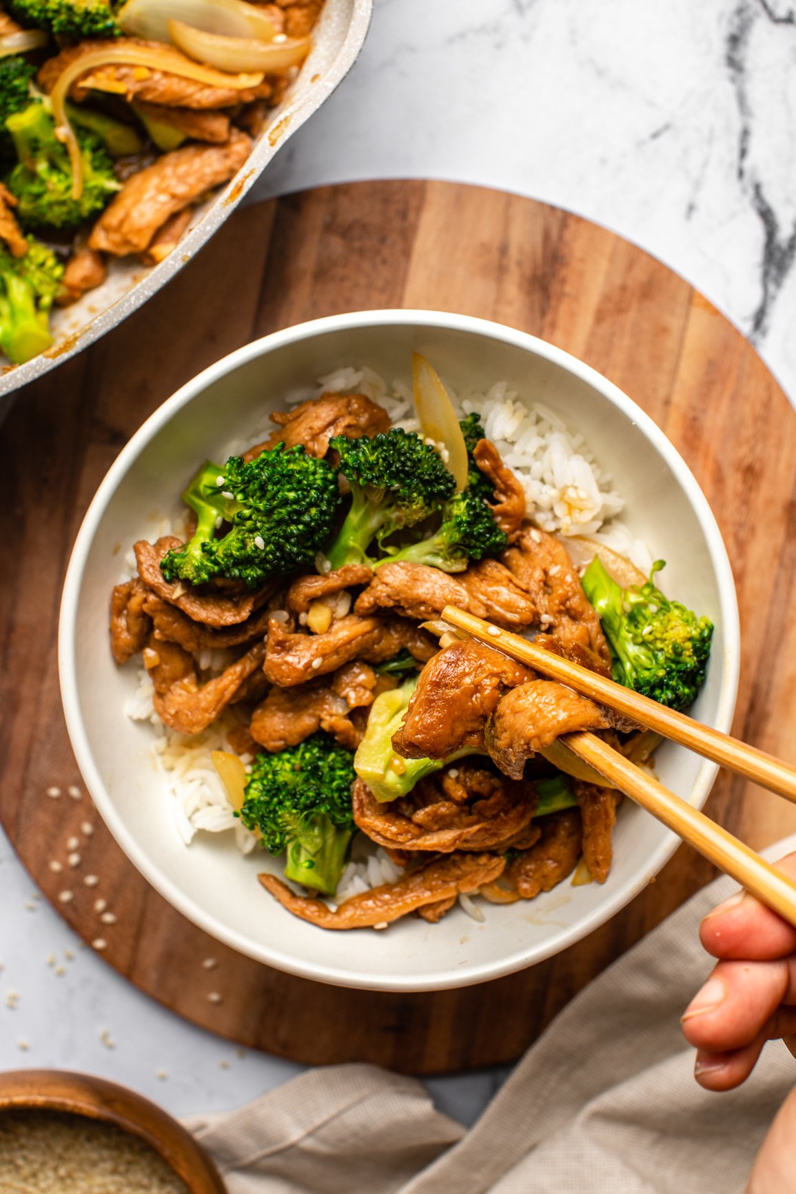 hand using chopsticks to pick up pieces of vegan "beef" from bowl of vegan beef and broccoli