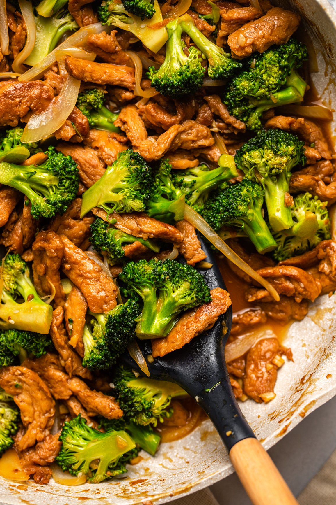 large pan of beef & broccoli with wooden spatula scooping a serving portion out of it