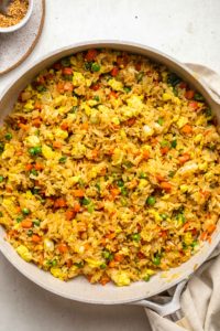 close up photo of cooked vegan fried rice with tofu egg in large white saute pan on white background