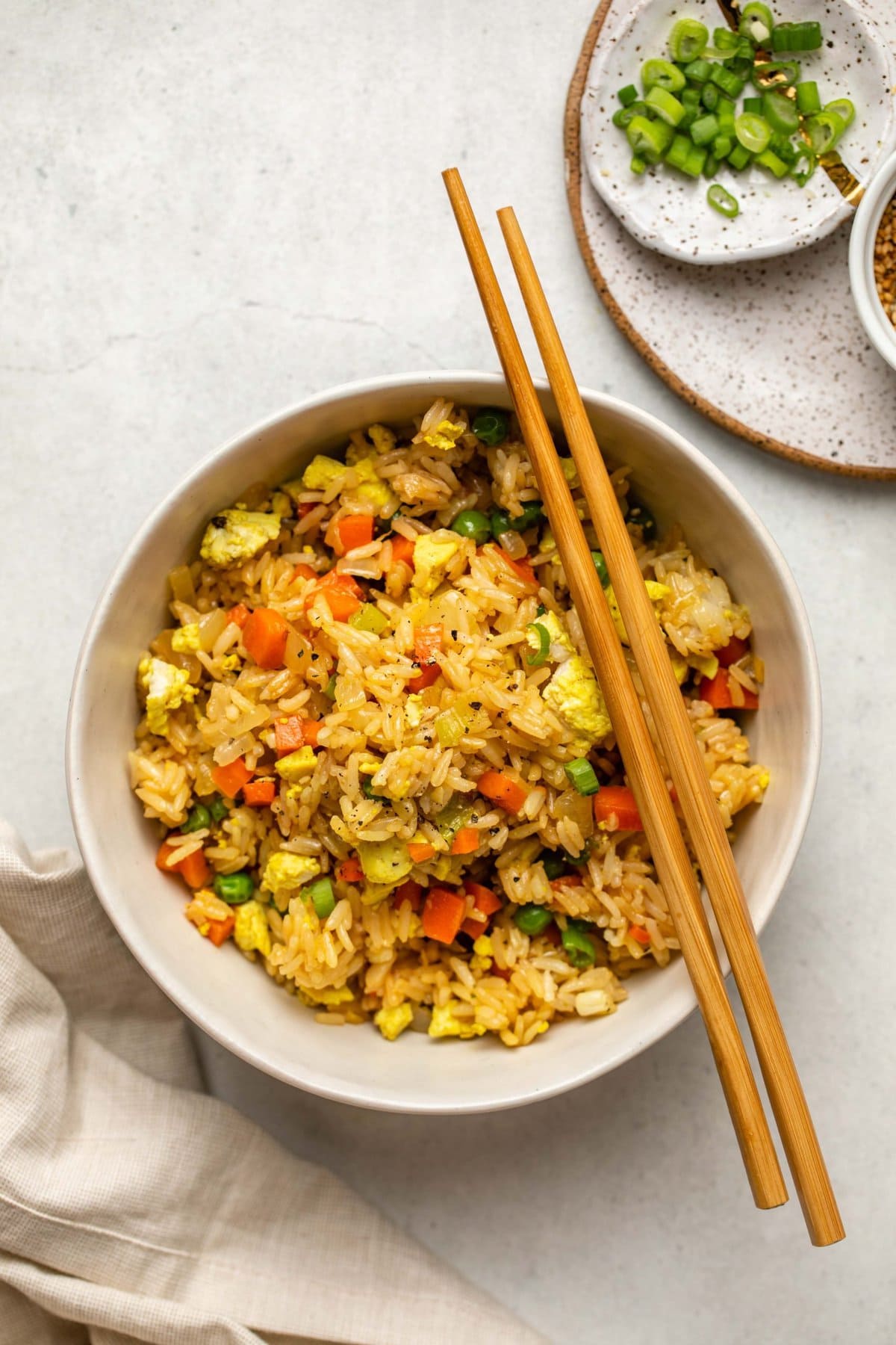 fried rice in white bowl with chopsticks and small dish of sliced green onions on the side