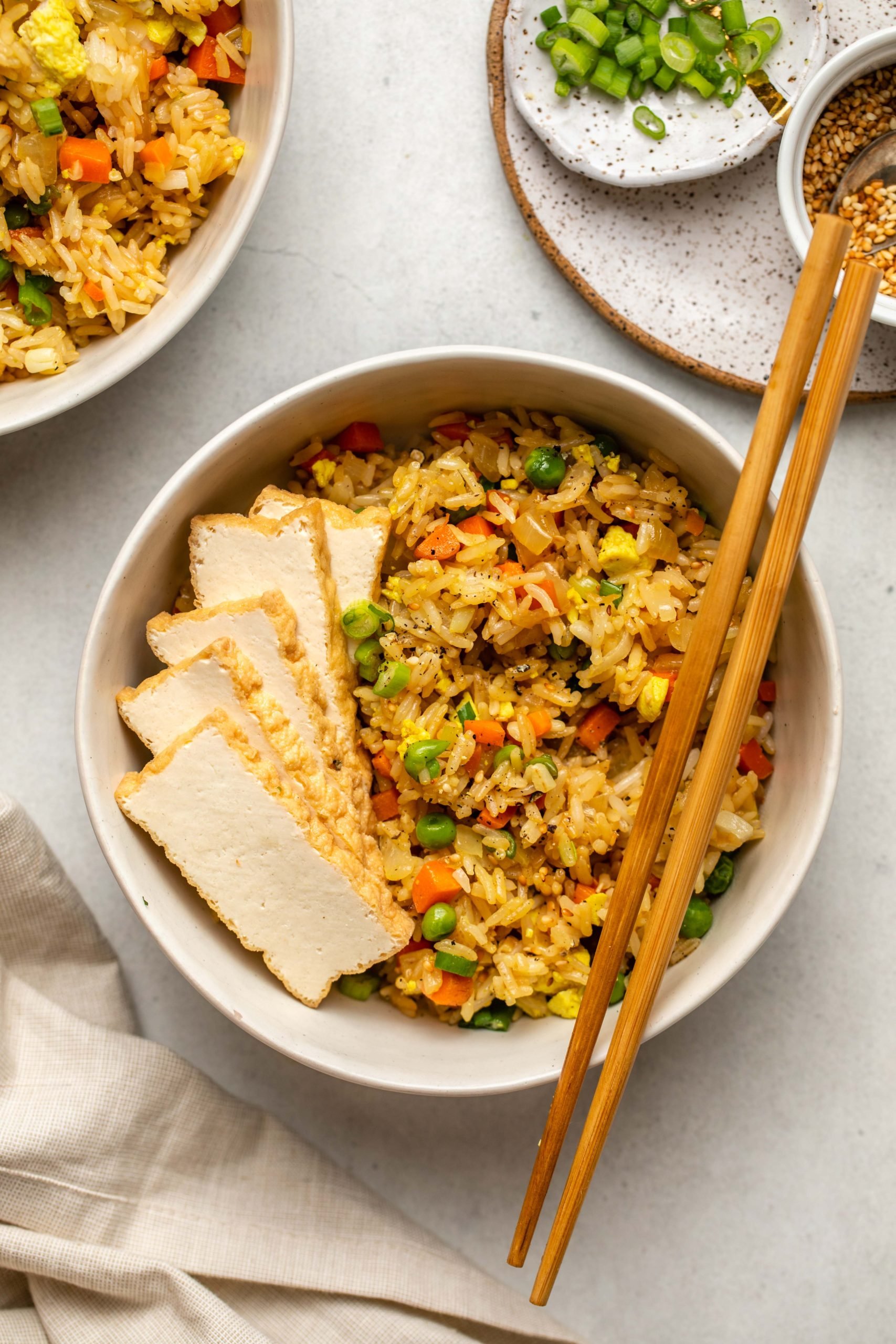 bowl of fried rice topped with sliced fried tofu and chopsticks on white background
