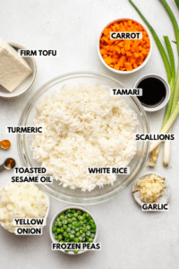 bowls of rice, carrot, peas, scallions, onion, tamari, garlic, toasted sesame oil, turmeric, and tofu on stone background