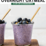 jar of blueberry overnight oatmeal on wood serving tray topped with fresh blueberries and hemp hearts. A gold spoon sits in the jar as well.