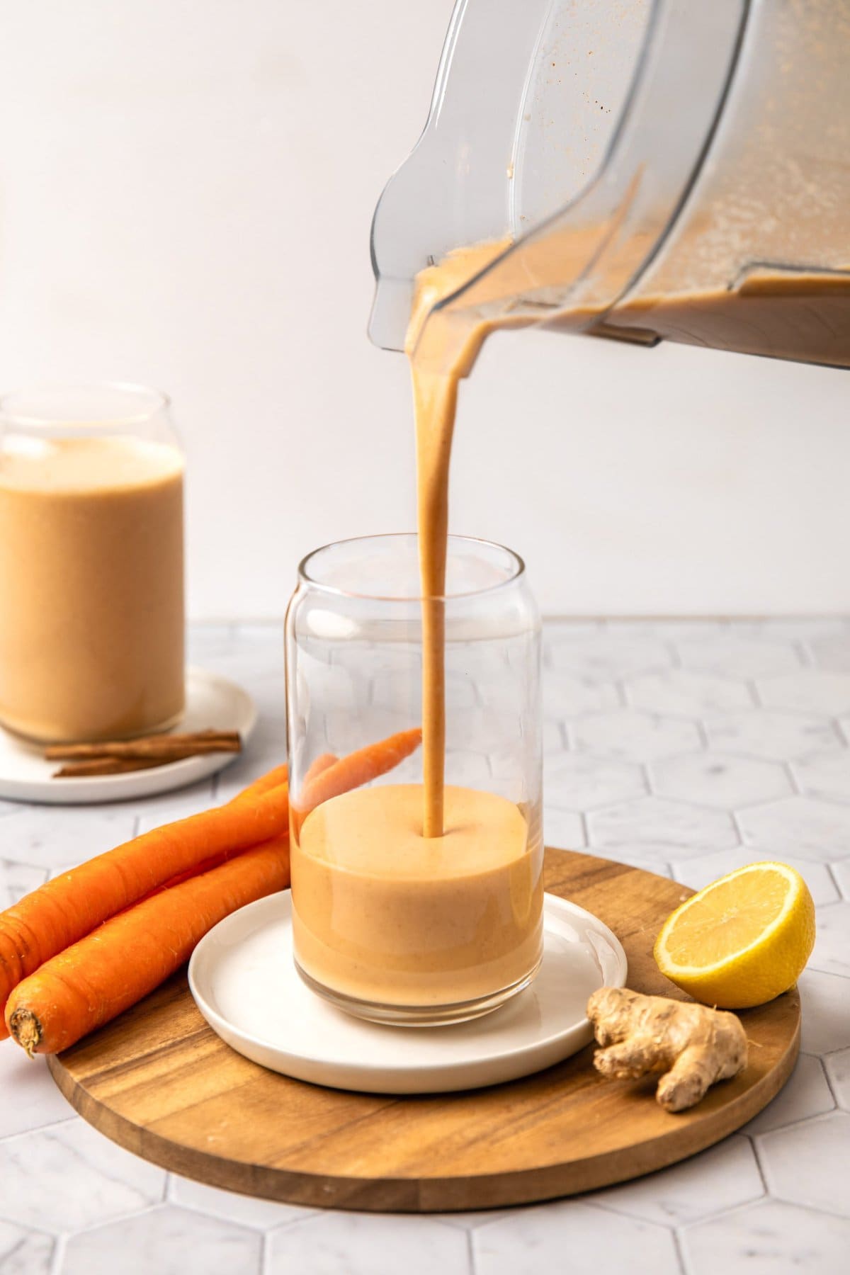 blender pouring carrot cake smoothie into tall glass that's resting on a wooden cutting board
