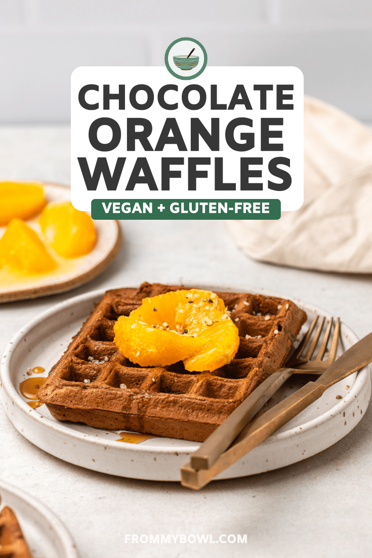 chocolate orange waffle topped with orange slices maple syrup and hemp hearts on small white plate with gold utensils 