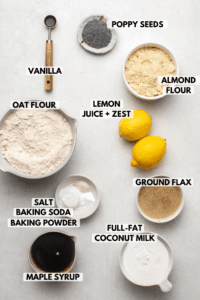 ingredients for lemon poppy seed care in small white bowls on stone background. Text labels read vanilla, poppy seeds, almond flour, oat flour, lemon juice + zest, ground flax, salt, baking soda, baking powder, full-fat coconut milk, and maple syrup