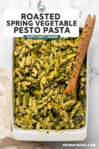 Roasted vegetable pesto pasta in white casserole dish with pasta mixed in and wooden serving spoon