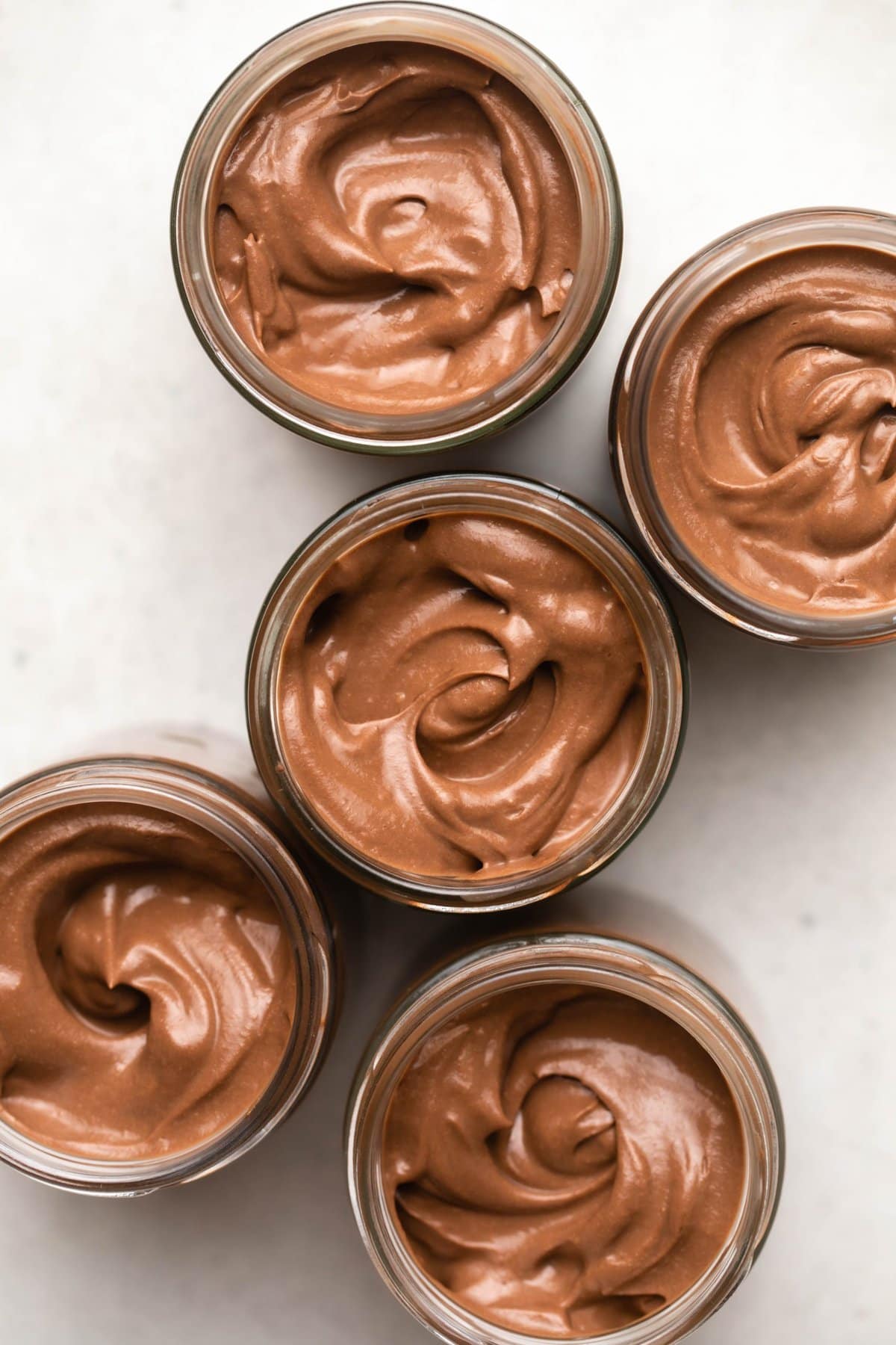 5 jars of chocolate pudding swirled with a spoon on stone background