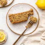 close up photo of slice of lemon poppy seed cake on white speckled plate with gold fork holding a bite of the cake to show texture