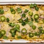 overhead photo of creamy green enchilada casserole topped with melted vegan cheese, red onion, jalapeno, and cilantro