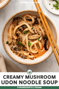 Creamy mushroom udon noodle soup in white speckled bowl topped with green onions and chopsticks on the side