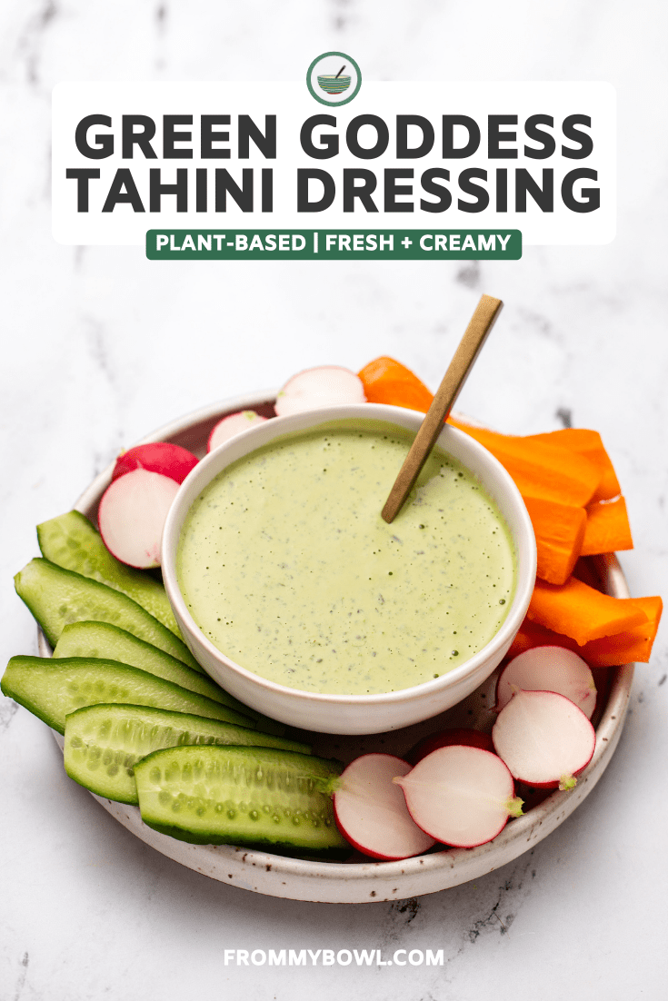 Green goddess tahini dressing in white bowl on plate of raw vegetables